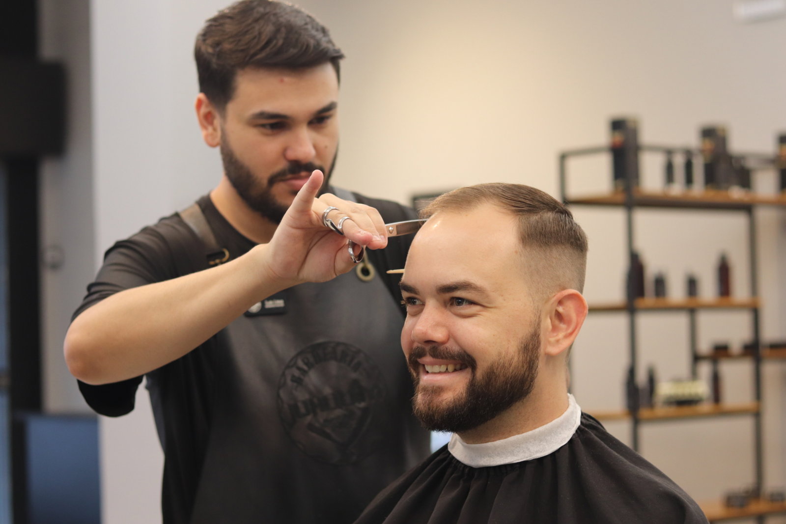 Corte na tesoura, com o cliente sorrindo na cadeira